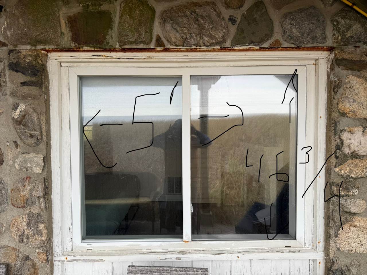Window in a stone wall with peeling paint and rot in the head casing and sill